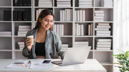 Businesswoman drinking coffee while checking finance document and typing business data on laptop