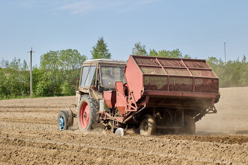Wheeled tractor with potato planter plants potatoes in field during spring sowing.