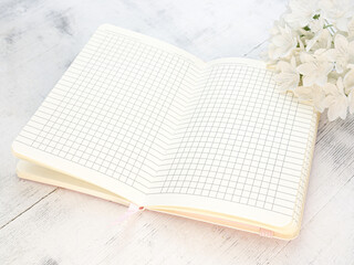 Still life, a bouquet of white flowers and a notebook on a light wooden background, space for text
