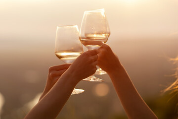 Close up on hands holding wine glasses on the picnic during sunset. Celebration concept.