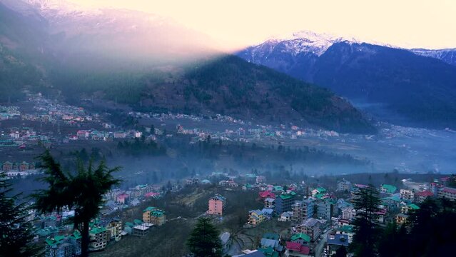 time lapse shot of monsoon clouds moving over snow covered himalaya mountains with the blue orange sunset sunrise light with town of kullu manali valley at the base of mountains