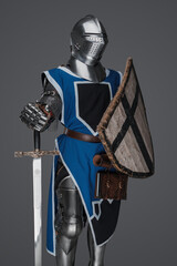 Blue surcoat-wearing medieval knight with sword and shield on gray background