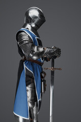 Medieval guard dressed in armor and blue surcoat holding a sword, standing in statue pose, against...