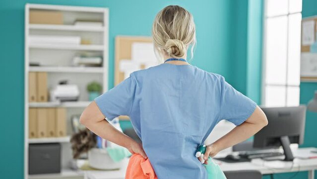 Young blonde woman professional cleaner holding cloth and sprayer standing backwards at the office
