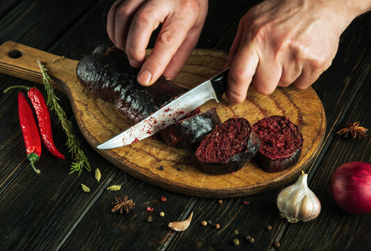 The chef cuts blood sausage with a knife on a cutting board for lunch. Close-up of a cook hands while slicing sausage
