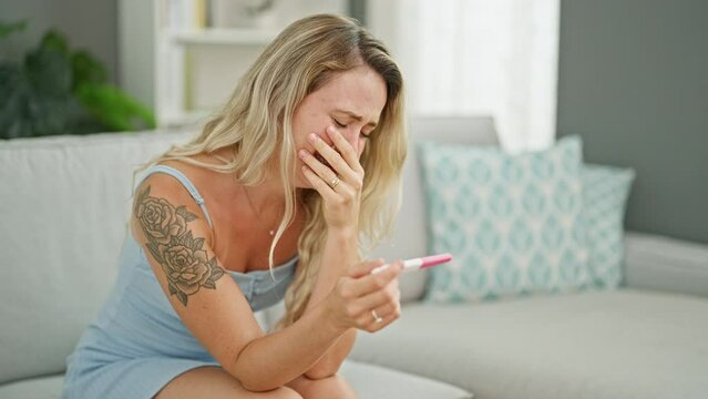 Young blonde woman holding pregnancy test crying at home