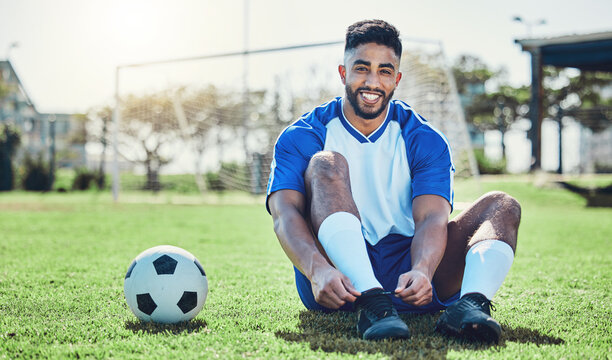 Sports, man or soccer player tie shoes for training, fitness games and performance on stadium field. Portrait, happy indian athlete or lace football sneakers on grass pitch to prepare for competition - Powered by Adobe