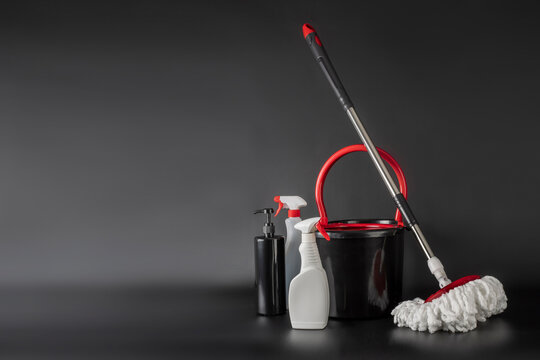 Cleaning concept mop and bucket. Cleaning products and spin mop with red details on the floor in the grey-black background