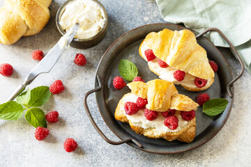 Healthy food dessert concept, french pastry. Tasty freshly baked croissants with cream cheese and raspberry on a stone background.