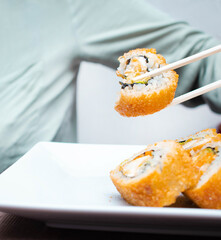 Comida japonesa o sushi de camaron sostenido por palillos chinos por la mano de una persona 