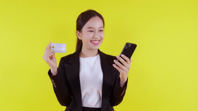 Portrait young asian business woman hold credit card and looking smart phone for shopping online isolated yellow background, businesswoman looking debit card and smartphone, financial concept.