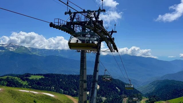 Modern rope way or cable way cabins with people against green valley, blue sky and mountain tops. Rosa Khutor, Soschi, Russia