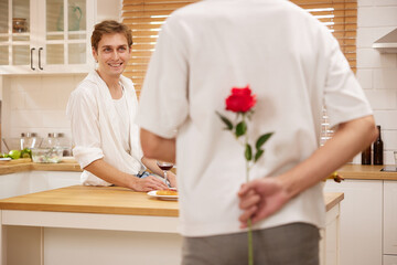 young gay couple looking at boyfriend and holding rose behind his back for surprise in the kitchen