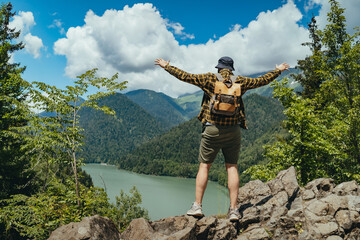 Hiking traveller man with backpack hands up enjoying beautioful view of Lake Ritsa in Abkhazia