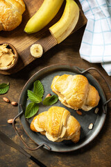 Healthy food dessert concept. French pastry. Tasty freshly baked croissants with peanut butter and banana on a rustic background. View from above.