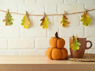 Coffee cup and pumpkin decoration on wooden shelf over brick wall background with autumn leaf...