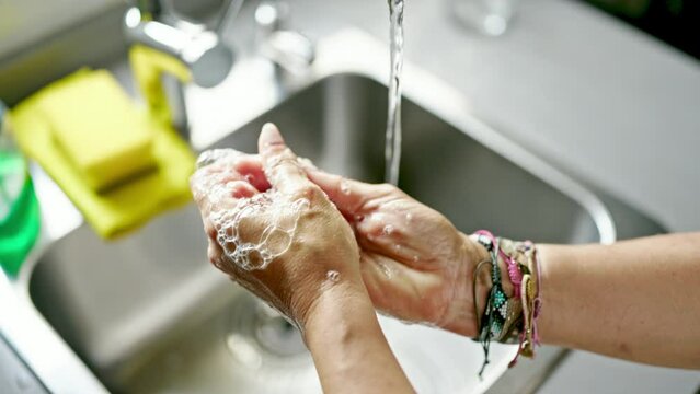 Middle age hispanic woman washing hands at the kitchen
