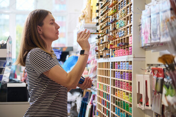 Caucasian young woman merchandiser, seller stacking pencils on shelves in school stationery store. Office supply shop