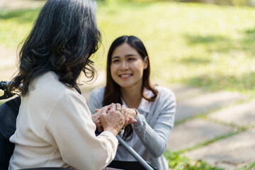 Asian senior woman in wheelchair with happy daughter. Family relationship retired woman sitting on wheelchair in the park age care at retirement home.