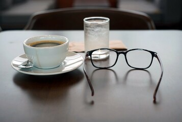 Cup of coffee and eyeglasses on a wooden table.