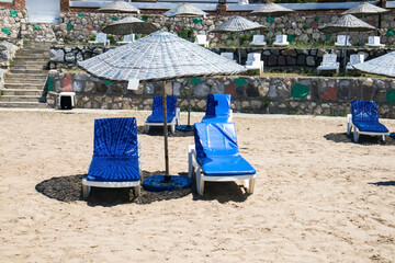 Fototapeta na wymiar Calm and a small beach with straw umbrellas and empty white sun loungers on the sand.Conceptual image of summer season