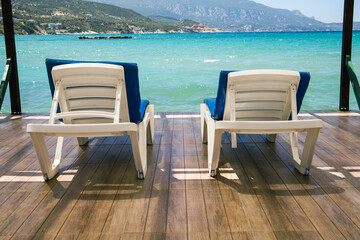Empty white sun loungers with blue cushions ready for guests on wooden pier with amazing sea view