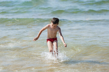 Fototapeta premium adorable school boy jumping in the water and enjoying the beach in summertime