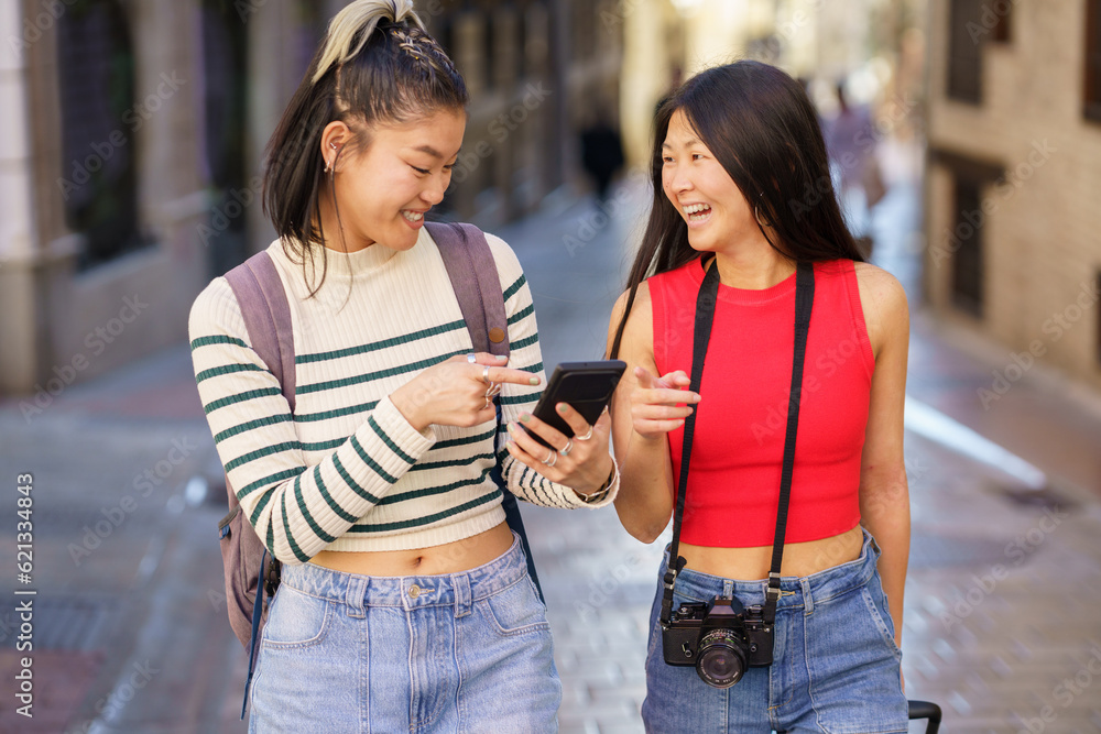 Wall mural Cheerful Asian travelers using cellphone while walking on urban street