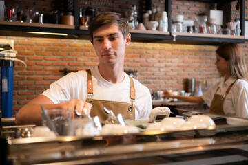 Fototapeta na wymiar Barista working in cafe. Portrait of young male barista standing behind counter in coffee shop.