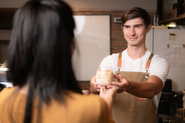 Barista holding a glass of cold latte coffee in his hands to customer