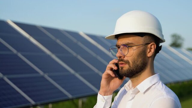 Confident engineer wearing safety hard hat, holding mobile phone, making a call. Engineer, worker, or architect working with Solar panel concept
