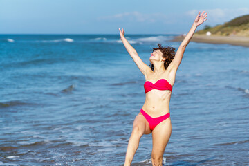 Fototapeta na wymiar Carefree woman in bikini with raised arms at beach