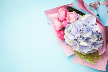 Bouquet of peony roses with hydrangea on a blue background, space for text. Top view.