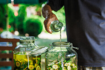 Making homemade walnut liqueur. Senior man pouring alcohol into jar with unripe nuts