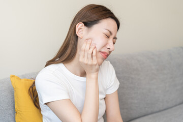 Closing eyes asian young woman hand touching cheek, face expression from toothache, tooth decay or...