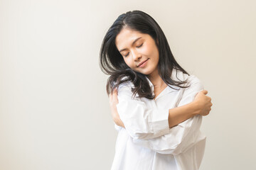 Smiling positive, hugging oneself happy asian young woman hands hug herself shoulders enjoy joyful, self hugging, self love and self care, face expression self esteem standing isolated on background.