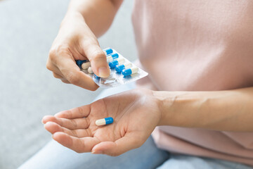 Sick ill asian young woman, girl hand taking tablet pill capsule out from blister pack, painkiller medicine from stomach pain, head ache, pain for treatment, take drug or vitamin at home, health care. - obrazy, fototapety, plakaty