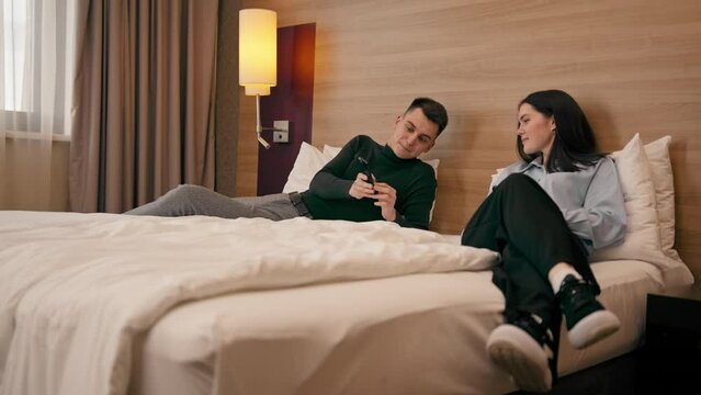 young couple in the room of a luxury hotel room lovers lying on the bed watching funny videos on the phone travel concept
