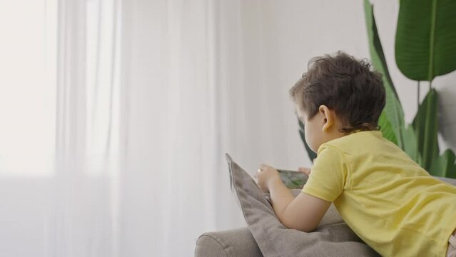Cute little kid relaxing at home using smartphone