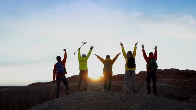 Back view at group of tourists friends together standing on mountain top in sunset light. Joy of achievement, happy travelers enjoy active lifestyle slow motion