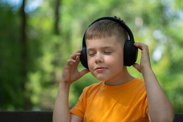 Outdoor portrait of a blond boy of eight years old with wireless headphones on his head.