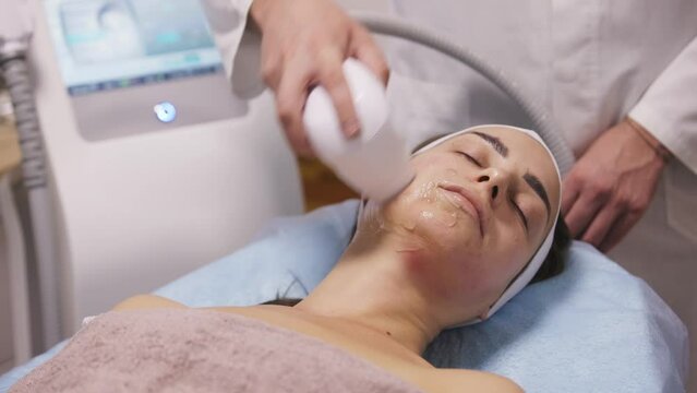 Microneedle RF lifting procedure. Hardware cosmetology. Beautician conducts a facial rejuvenation procedure for a brunette woman