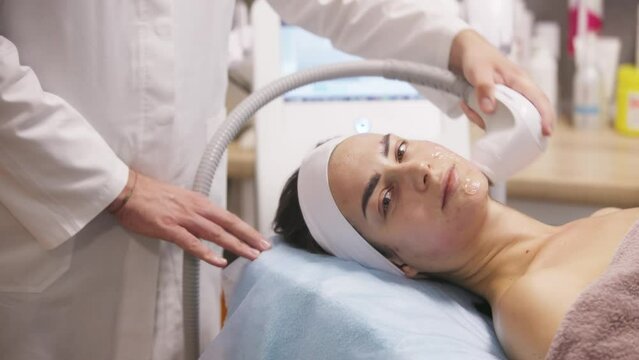 Radiofrequency facial skin lifting. Hardware cosmetology RF lifting procedure and hardware facial massage. Rejuvenation, skin care in a beauty salon. Man doctor cosmetologist and girl in spa clinic.