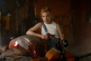 Obraz na płótnie Canvas Young woman doing hard job at motorcycle garage using grinder