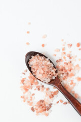 Fototapeta na wymiar Pink Himalayan coarse crystalline salt in brown wooden spoon on white background top view with copy space
