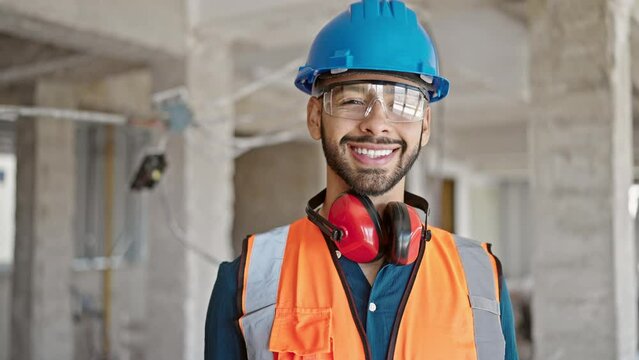 Young hispanic man builder smiling confident wearing hardhat at construction site