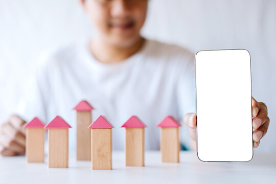 A young man is assembling a condo model while showing a blank white smartphone screen to fill in some text.