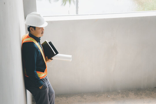 A foreman wearing a hard hat stands holding a blueprint. Supervising and inspecting the construction project of the building to be successful as planned.