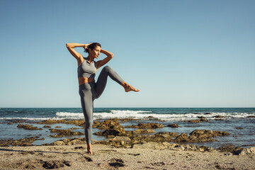 Fototapeta na wymiar a beautiful brunette girl in gray leggings is engaged in fitness on the sand against the background of the sea