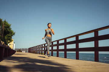 Fototapeta premium beautiful brunette girl in gray leggings runs on the seashore